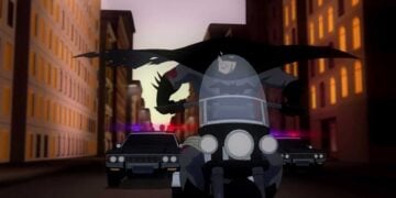 Animated Batman speeding on a motorcycle with police cars in pursuit through Gotham City in Batman: Year One