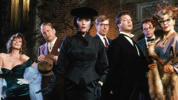 The cast of Clue (1985) posed outside the mansion — Miss Scarlet, Mrs Peacock, Mr Green, Professor Plum, Colonel Mustard and Mrs White