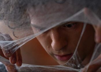 Tom Holland as Peter Parker peers through a web-covered face in Spider-Man: Brand New Day