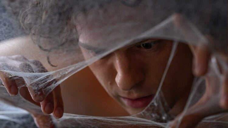 Tom Holland as Peter Parker peers through a web-covered face in Spider-Man: Brand New Day