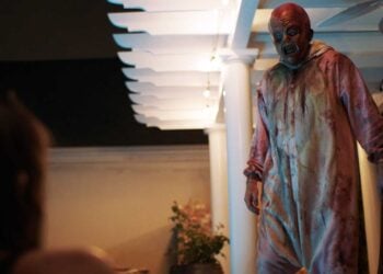 Big Baby slasher villain stands on a porch at night in a bloodstained onesie, wielding an axe, in Spider One's 2026 horror film.