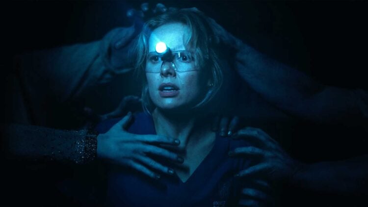 Amelia Eve as Gemma wearing a headlamp, reaching hands grabbing at her in the dark in Insidious: Out of the Further
