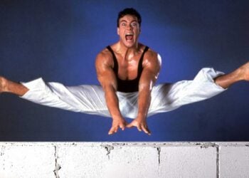 Jean-Claude Van Damme mid-air performing a split jump over a wall in a promotional photo